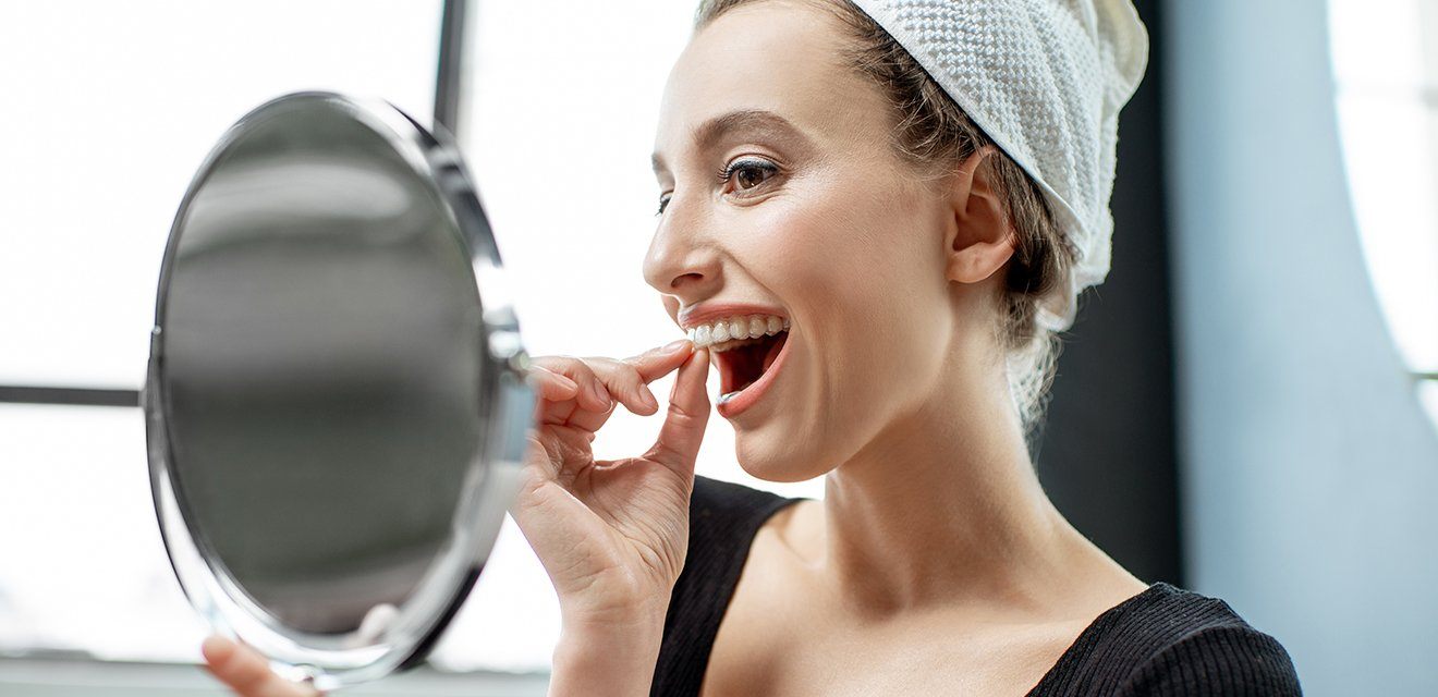 woman looking at herself putting in invisalign