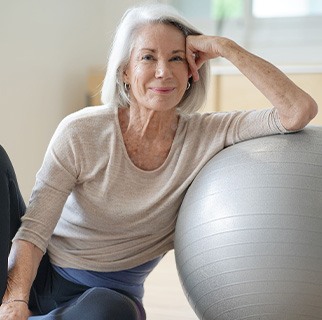 Senior woman smiling while resting against balance ball
