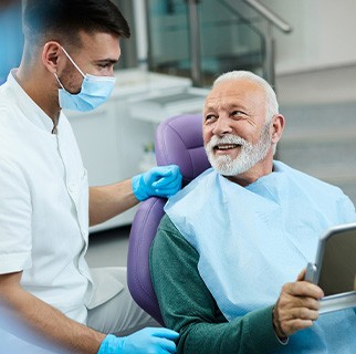 Senior patient looking at dentist while holding small mirror