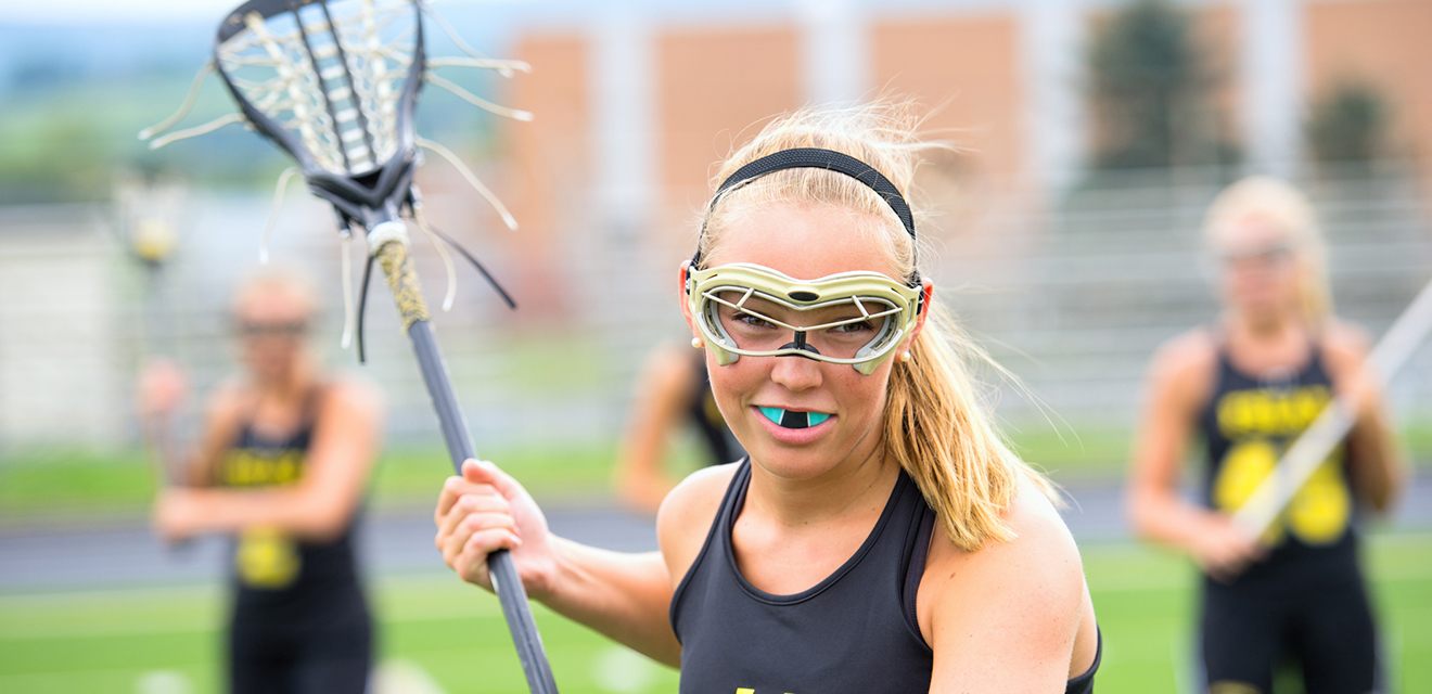 girl playing lacrosse with mouthguard in