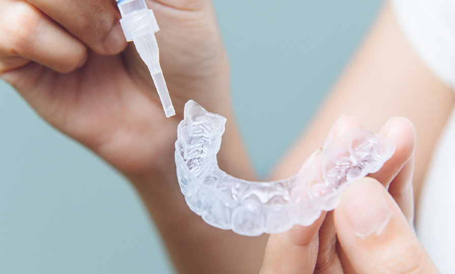 a person placing teeth whitening gel in an oral applicator