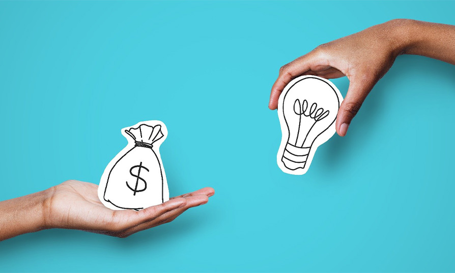 hands holding two paper cutouts, one is a bag of money and one is a lightbulb