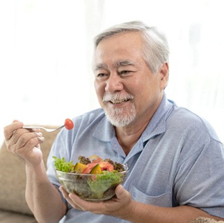 Man eating salad with dental implants in Denver
