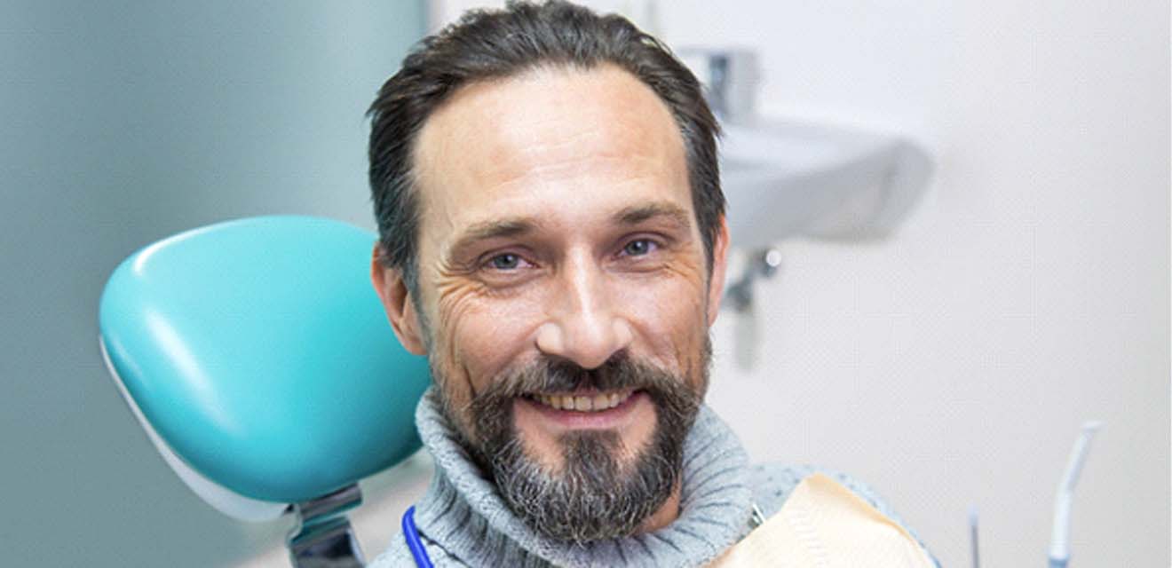 Man with beard smiling while sitting in dental chair