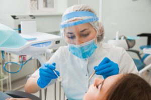 Dentist in Denver wearing mask while cleaning patient's teeth