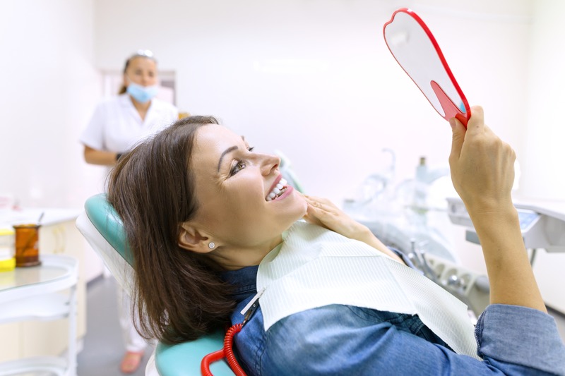 Patient smiling in mirror with cosmetic dentist in background